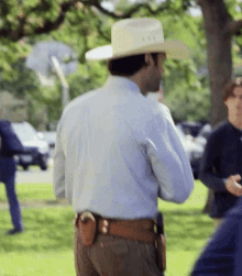 a man wearing a cowboy hat is standing in the grass