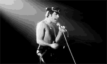 a man without a shirt is singing into a microphone on a stage .