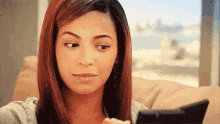 a woman is sitting on a couch looking at her phone and making a funny face .