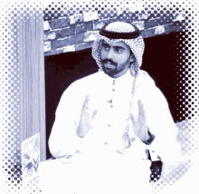 a man with a beard wearing a white shirt and a head scarf is sitting at a table