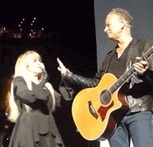 a man holding a guitar next to a woman who is holding her hand up