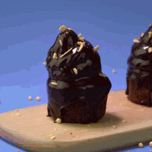 a chocolate covered cupcake with nuts on top is on a wooden cutting board