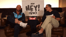 two men sitting in front of a sign that says hey