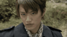a young man wearing a scarf and a black jacket looks at the camera