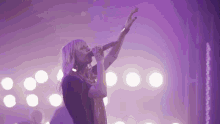 a woman singing into a microphone in front of a purple background