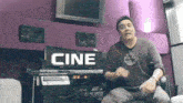 a man is sitting in front of a sign that says cine on it