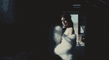 a woman in a white fur coat stands in the dark