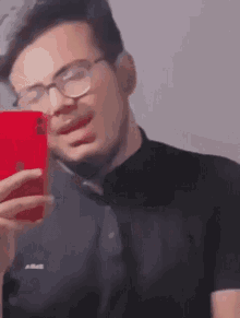 a man wearing glasses is taking a selfie with his red iphone
