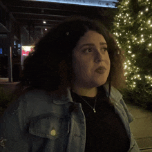 a woman in a denim jacket stands in front of a sign that says what