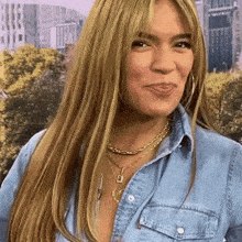 a woman with long blonde hair is wearing a denim shirt and a gold necklace