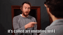 a man with a beard is pointing at himself in a mirror and says it 's called art imitating wife