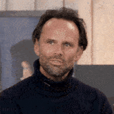 a man with a beard is wearing a black turtleneck sweater with the word yonneli on the bottom
