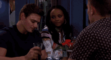 two men and a woman are sitting at a table with a glass of beer in front of them