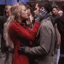 a woman in a red coat is kissing a man in a grey jacket .