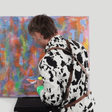 a man wearing a cow print jacket is painting a picture