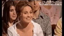 a woman in a white shirt is sitting in a crowd of people and smiling .