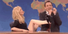 a man and a woman are sitting at a desk with a woman 's leg up .