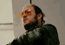 a man with a beard and sunglasses is wearing a camouflage jacket .
