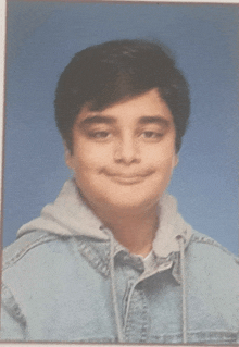 a young man wearing a denim jacket and a hoodie smiles for the camera