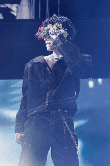 a man wearing a black jacket and black pants holds flowers in front of his eyes