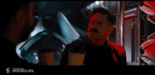 a man with a mustache is standing next to another man in a dark room .