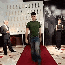 a man is walking down a red carpet in front of a wall of statues of celebrities .