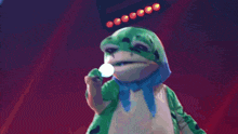 a green and white frog with a blue scarf around its neck is on a stage