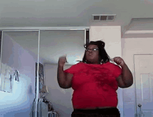 a woman wearing glasses and a red shirt is dancing in a bedroom