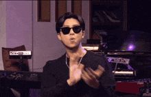 a man wearing sunglasses and a black shirt is standing in front of a keyboard that says s90