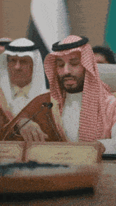 a man in a keffiyeh is sitting at a table with a name plate that says chairman