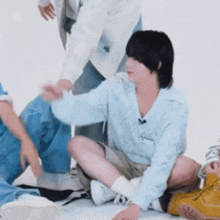 a young man is sitting on the floor with his legs crossed while a group of people are standing around him .