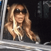 a woman wearing sunglasses is sitting in a car with her mouth open .