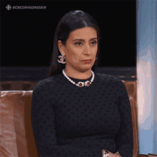 a woman wearing pearls and chanel earrings is sitting on a couch
