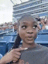 a girl in a ponytail is pointing at something in a crowded stadium .