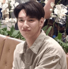 a young man is sitting on a couch in front of flowers and plants .