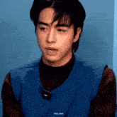 a close up of a young man wearing a blue vest and a brown turtleneck