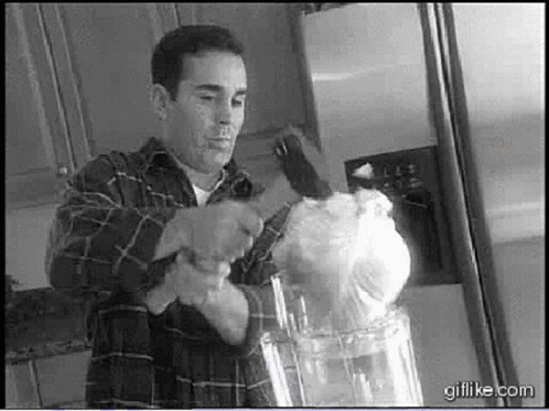 A gif of a "joe everybody" looking dude using a sledgehammer to smash a large head of iceberg lettuce into a food processor. his demeanor is 100% unironic. the scene is a parody of an infomercial