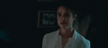 a woman in a white shirt is standing in a dark room with her eyes closed .