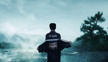 a man wearing a jacket that says jh jung stands in front of a river