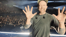 a man wearing a hat and ear buds waves his hands in front of a crowd