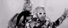 a black and white photo of a man wearing sunglasses and a camouflage shirt .