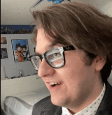 a man wearing glasses and a leather jacket is smiling in a room .