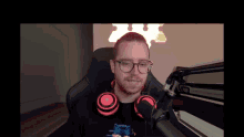 a man wearing glasses and red headphones is sitting in front of a microphone .
