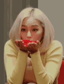 a woman in a yellow sweater is blowing a kiss with a red rose in her hands .