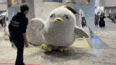 a man wearing a black staff shirt stands next to a stuffed bird mascot