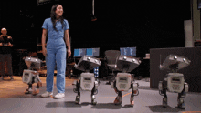 a woman in a blue scrub suit stands next to a row of robots