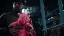 a man is holding a pink teddy bear in a dark room .