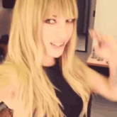 a woman with long blonde hair and bangs is smiling and waving .
