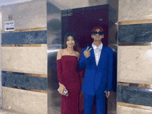 a man in a blue suit stands next to a woman in a red dress in front of an elevator