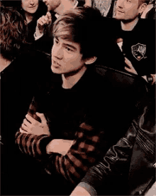 a young man in a plaid shirt is sitting in a crowd .